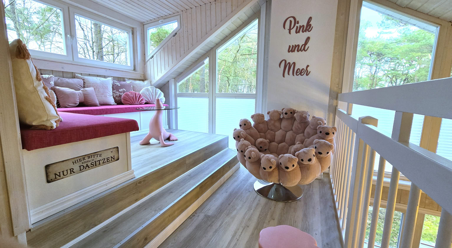 Gemütlicher Dachbodenraum mit einem Fenster, einer rosa Sitzbank, einem runden Sessel mit Plüschkissen und der Aufschrift "Pink and More" an der Wand.